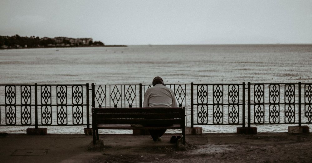 A sad man sitting alone on a bench by the seaside needing mental health support