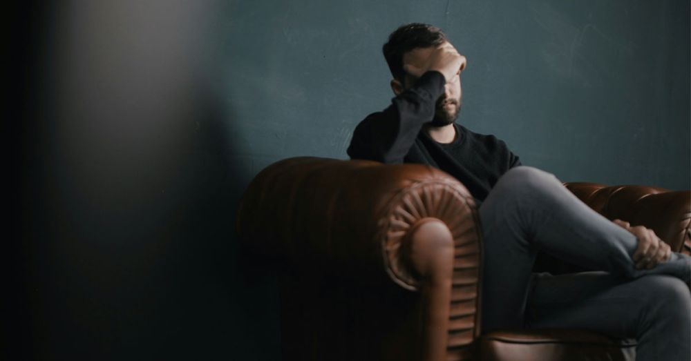 A man sitting on an armchair with his hand on his face, needing mental health support.