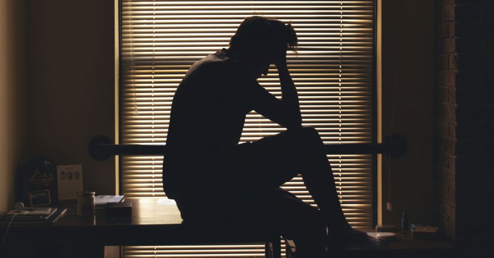A man sitting thoughtfully by a window needing mental health help